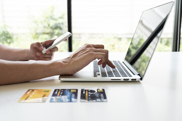 Closeup hand of a men is holding mobile phone and using computer notebook for shopping online.