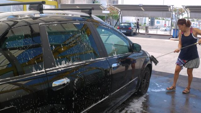young caucasian woman rinsing and spraying her car clean at self service car wash