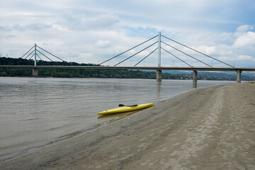Yellow kayak left on the bank of the river with bridge in the background