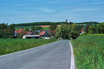 Empty asphalt road surrounded with fresh green grass. Spring landscape of a little bavarian village Lempertshausen, Germany. Beautiful european nature with blue sky in middle springtime.
