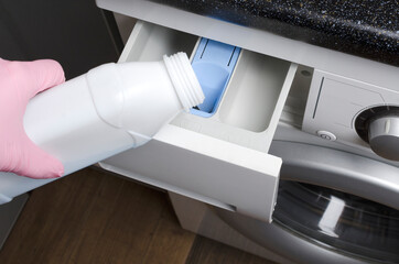 Woman wearing protective pink gloves and pouring liquid detergent into the washing machine.Household routines