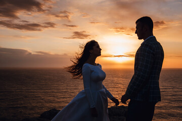 Silhouette of a loving couple at sunset, with sea background. Bride and groom looking at each other. Concept of family, wedding, and honeymoon