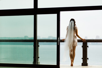 The bride stands with her back to her robe, leaning on the railing and looking at the lake.