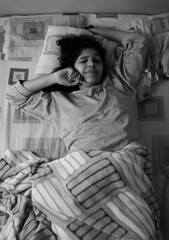 Woman in bed wrapped up to the waist, waking up and stretching to start her day