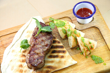 Medium-roasted steak cut into pieces on a wooden board with sauce and seasonings. Delicious steak. Beef steak medium rare on vegetable cushion. Beef steak on wooden plate.