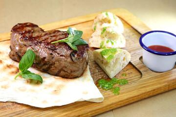 Medium-roasted steak cut into pieces on a wooden board with sauce and seasonings. Delicious steak. Beef steak medium rare on vegetable cushion. Beef steak on wooden plate.