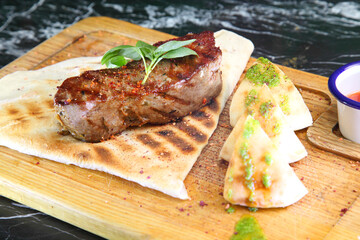 Medium-roasted steak cut into pieces on a wooden board with sauce and seasonings. Delicious steak. Beef steak medium rare on vegetable cushion. Beef steak on wooden plate.