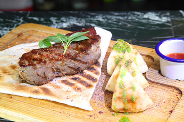 Medium-roasted steak cut into pieces on a wooden board with sauce and seasonings. Delicious steak. Beef steak medium rare on vegetable cushion. Beef steak on wooden plate.