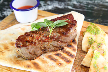 Medium-roasted steak cut into pieces on a wooden board with sauce and seasonings. Delicious steak. Beef steak medium rare on vegetable cushion. Beef steak on wooden plate.