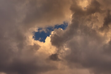 Piece of blue sky, surrounded by white clouds shaded by gray