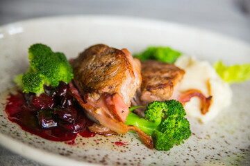 meat medallions in bacon with broccoli and cherries on a light plate beautifully canned