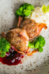 meat medallions in bacon with broccoli and cherries on a light plate beautifully canned