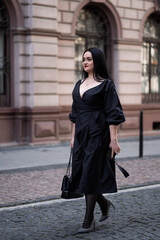 Autumn fashion outdoor. The girl with red lips in fashionable stylish black dress, autumnal lifestyle on the background of blurry yellow-green trees in the park. Vertical