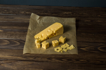 Maasdamer cheese. diced cheese in wrapping paper on an old black wooden table.