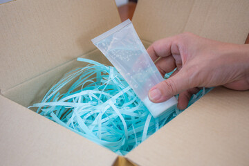 An Asian woman is holding a tube of alcohol gel from a paper package box with blue paper protection.