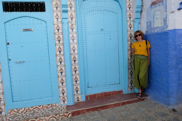 Pretty smiling woman standing near ornamented door in the blue city of Chefchaouen, Morocco.