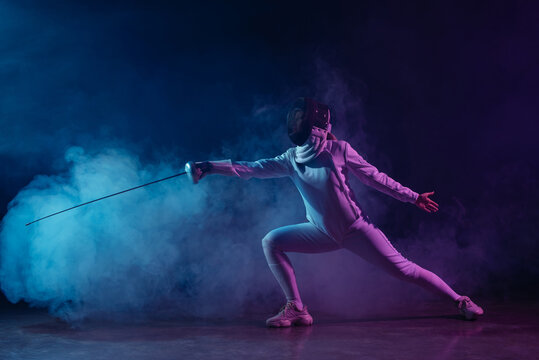 Swordswoman fencing with rapier on black background with smoke and lighting