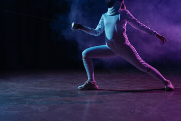 Cropped view of swordswoman fencing on black background with smoke and lighting