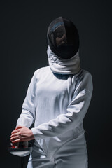 Fencer in fencing suit and mask holding rapier isolated on black