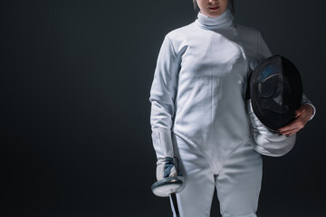 Cropped view of fencer holding fencing mask and rapier isolated on black
