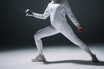 Cropped view of fencer in fencing suit training with rapier on white surface on black background