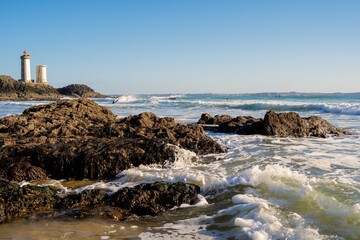 Wave covering sand and rocks on the beach with the Petit Minou lighthouse in the background near Brest in Brittany, France