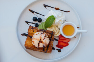 Close up Honey Toast serve with Vanilla ice-cream, Whip cream, Sliced bananas, and strawberries on the white plate.