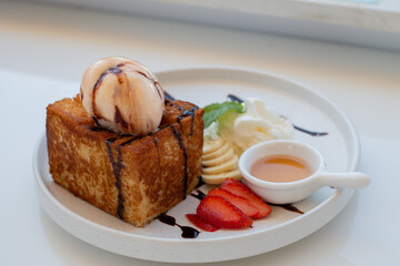 Close up Honey Toast serve with Vanilla ice-cream, Whip cream, Sliced bananas, and strawberries on the white plate.