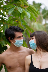 Young happy couple looking at each other with surgery protective mask during coronavirus summer holiday