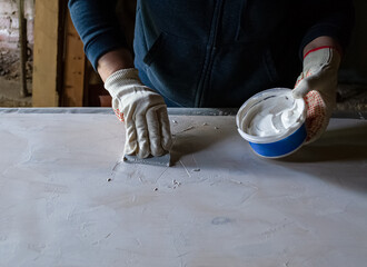 Woman putting plaster on flat board with rubber spatula making photography backdrop for a DIY...
