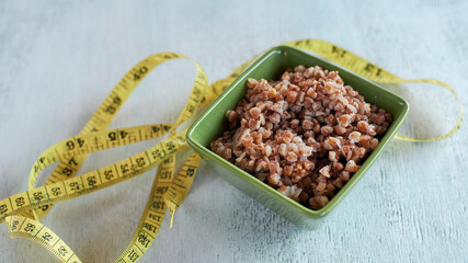 Cooked buckwheat porridge. Porridge in a bowl on the table. And a measuring tape in centimeters. Buckwheat diet concept.. Top view