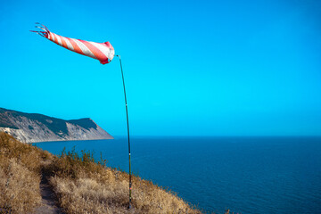 Red and white striped windsock on the seashore. The windsock is developing by the wind on the sea...