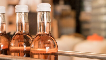 Close-up of rose wine bottles with white screw caps in an automated filling line in a german...