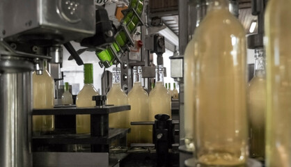 Close-up of just filled white wine bottles in a filling line which are just getting their green sealing screw cap in a traditional german winery.