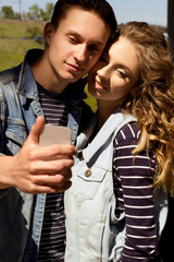 Two young people man and woman wearing jeans outdoors doing selfie