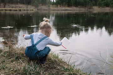 Little girl in rubber boots catches and feeds fish on the river in a jar