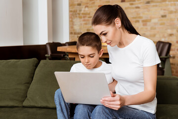 Mother and son using laptop on couch at home