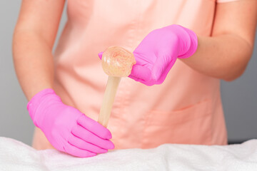 Cosmetologist hands are holding liquid sugar paste or wax during depilation procedure in salon.