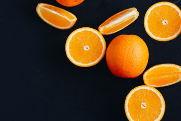 Halves and slices of fresh juicy oranges on black textured background with empty place for text.