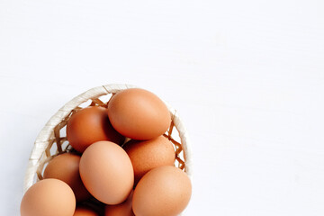 Brown chicken eggs in a straw basket on white wooden background. Top view with copy space.