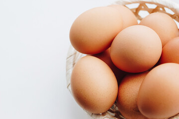 Brown chicken eggs in a straw basket on white wooden background.