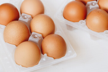 Brown chicken eggs in plastic container on white wooden background.