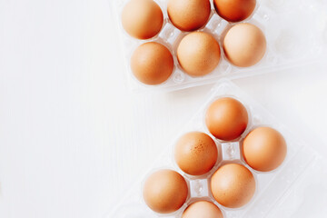 Brown chicken eggs in plastic container on white wooden background. Top view with copy space.