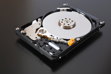 A disassembled open hard disk drive HDD of a computer or laptop lies on a dark matte surface. Close-up. IT&C. Illustration: computer hardware and equipment. Macro