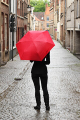 An unrecognizable women with a red umbrella practicing social distancing by walking alone down an empty street during the Coronavirus (covid-19) pandemic. 