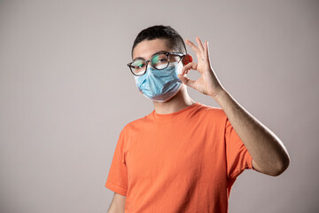 Ragazzo giovane con mascherina protettiva facciale, occhiali da vista neri e shirt arancione indica...