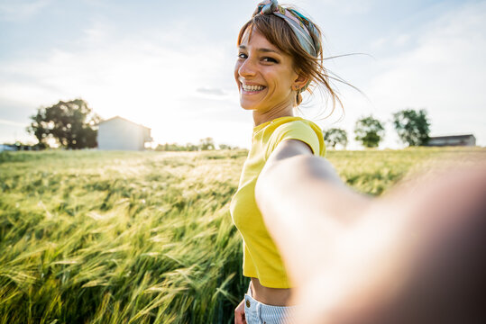 Happy millennial beautiful woman taking a selfie portrait with smartphone on a wheat field at summer. Portrait of a smiling girl looking at the camera