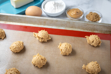 Raw peanut butter cookies on a silicon mat beside baking ingredients