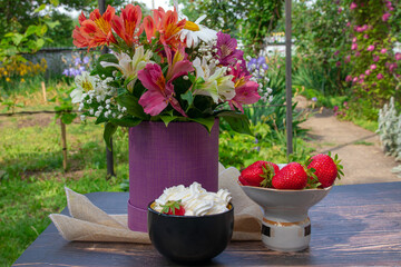 Bouquet of flowers on an old table. Strawberries in a vase. Strawberries and cream. Flowers and strawberries. Spring breakfast in the fresh air.