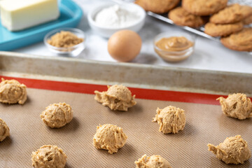 Cookie dough balls on a baking sheet with recipe ingredients in the background